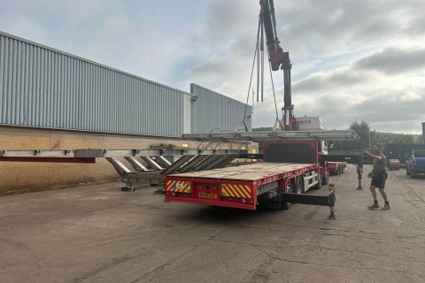 Crane lifting a long steel structure in an outdoor yard